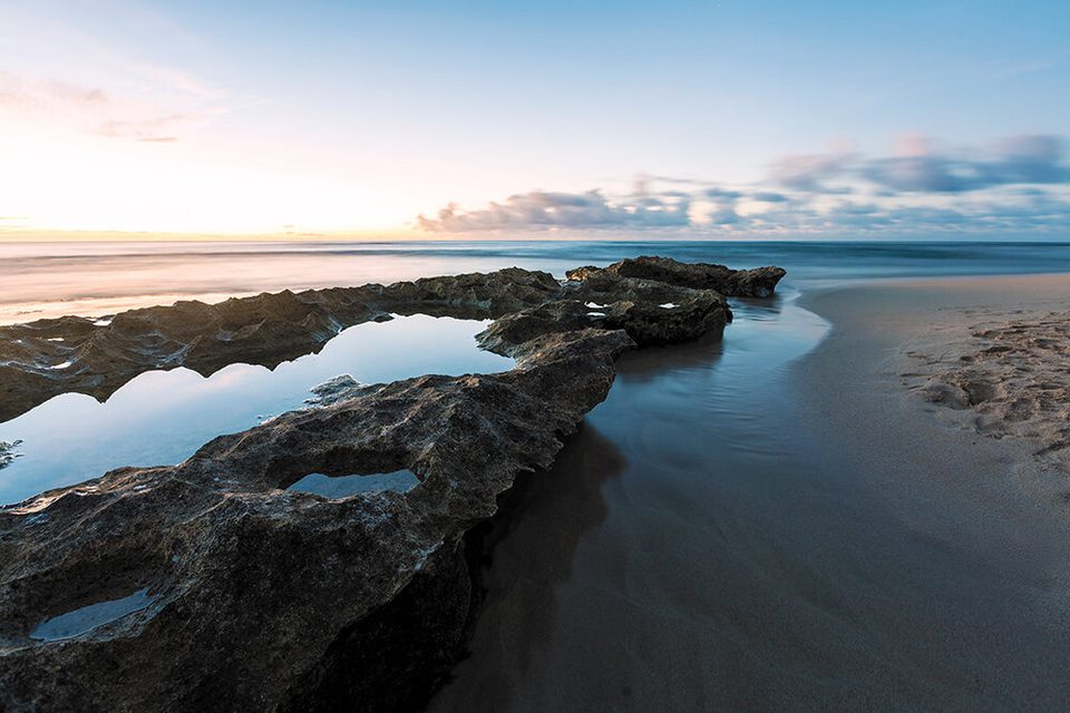 Silky water flowing over dark reef at Papailoa Beach on the North Shore at sunset
